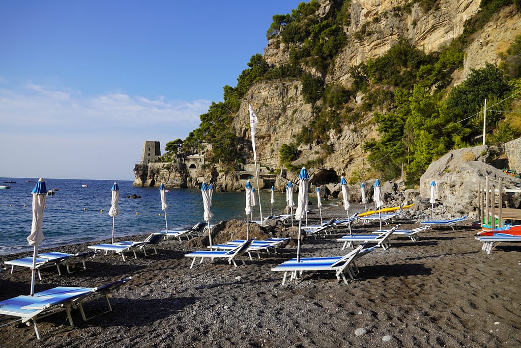 Fornillo Beach in Positano, Italy. Chairs line the beach, and a fort sits on the edge of the cliffs.