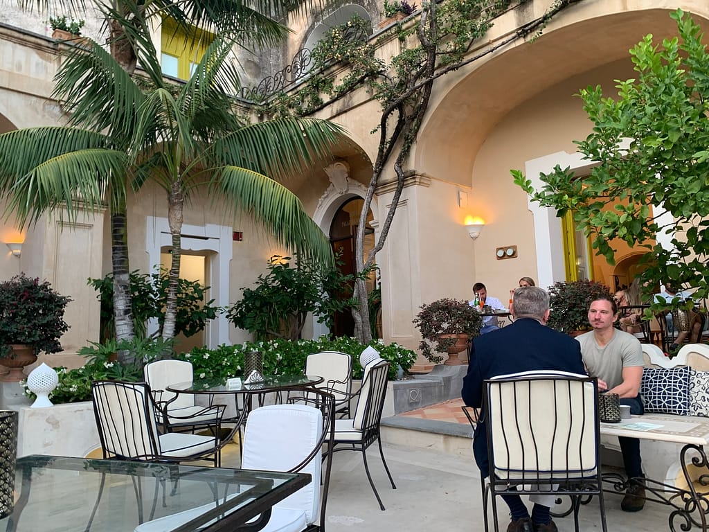 Outdoor courtyard at Palazzo Murat in Positano, Italy. People sit at tables listening to live music in the early evening.