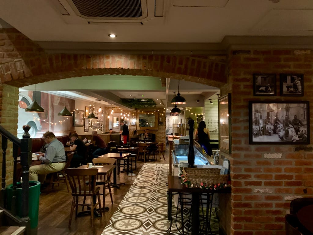 Interior of Bella Italia in York, England. The restaurant is a mix of modern and rustic, with woods, geometric tile, and exposed brick.