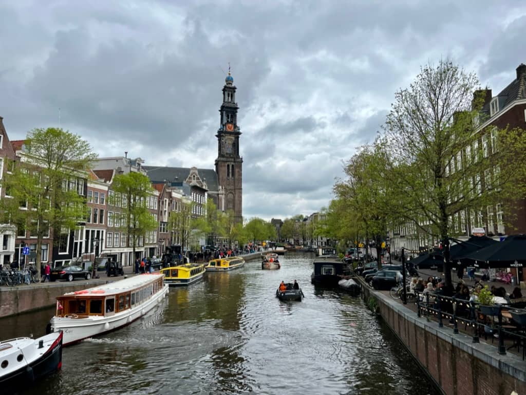 A canal in Amsterdam. A church bell tower stands along the canal-side